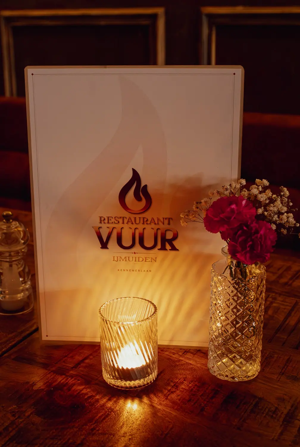 De VUUR-menukaart rechtop op tafel naast een kaars en bloemen.