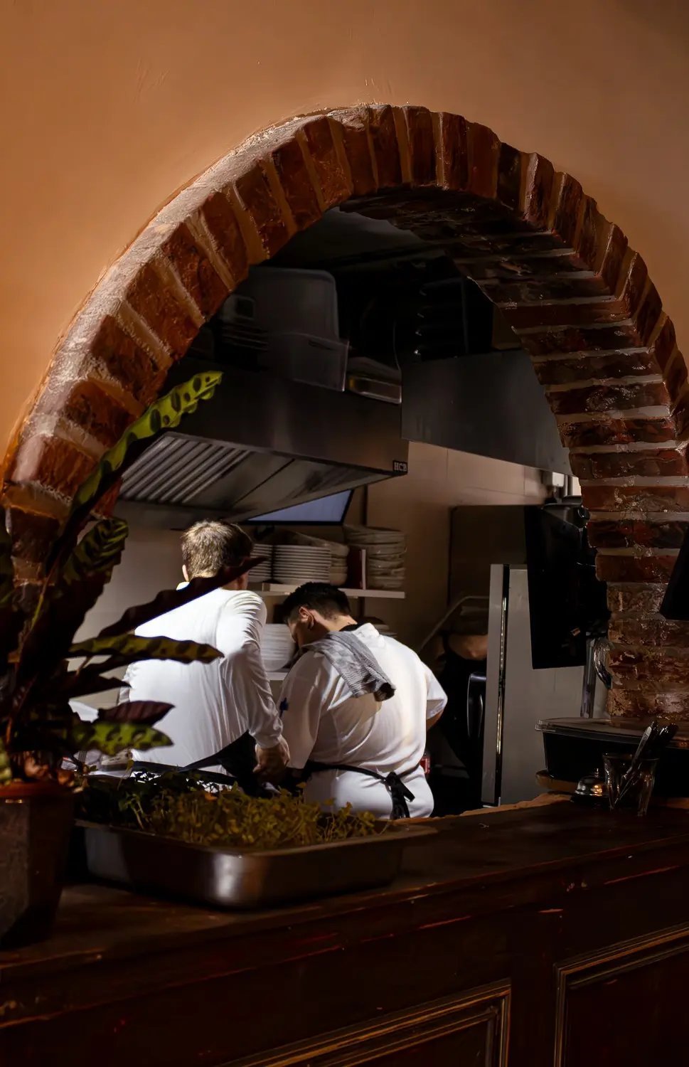 Koks aan het werk in de open keuken, gezien door de bakstenen boog.